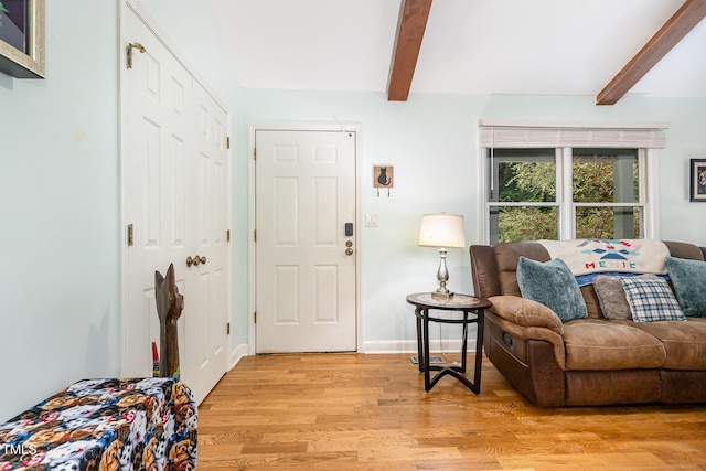 living area featuring beamed ceiling, light wood-type flooring, and baseboards
