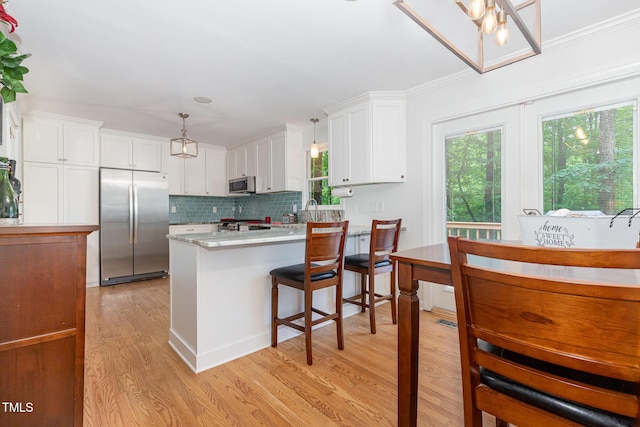 kitchen featuring appliances with stainless steel finishes, light wood-type flooring, white cabinets, light countertops, and decorative light fixtures