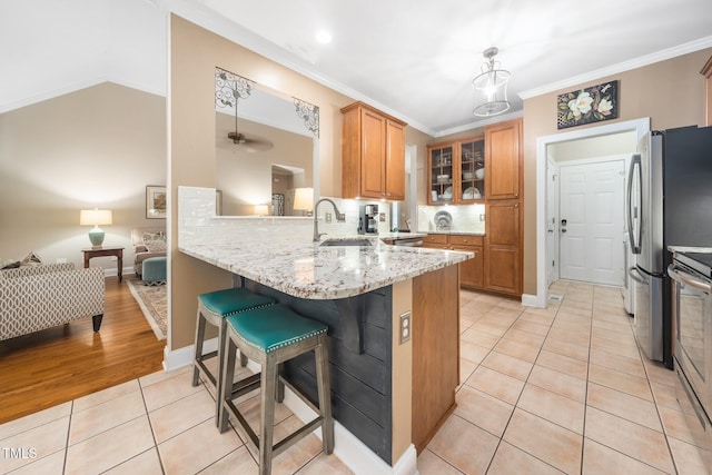 3916 Rustic Mill Dr, Apex, NC 27539 - kitchen featuring a sink, light tile patterned flooring, brown cabinetry, a kitchen bar, and appliances with stainless steel finishes