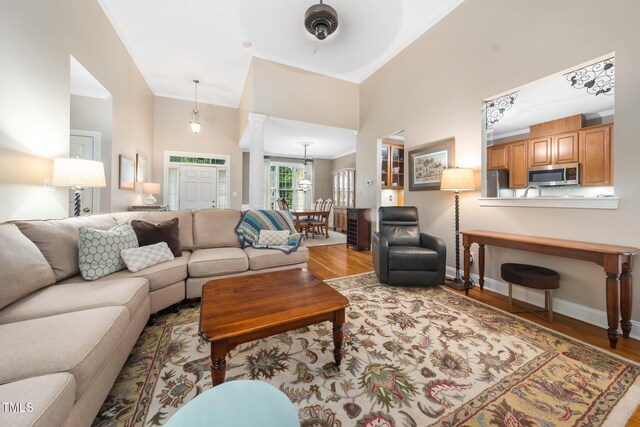 3916 Rustic Mill Dr, Apex, NC 27539 - living room featuring wood finished floors, baseboards, a towering ceiling, ornamental molding, and decorative columns