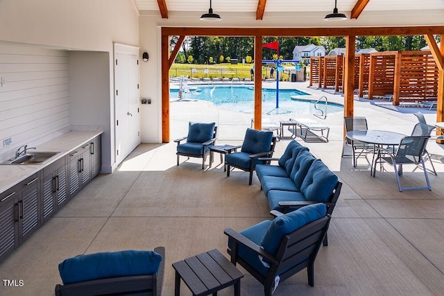 view of patio / terrace featuring a sink, outdoor lounge area, ceiling fan, a community pool, and an outdoor kitchen