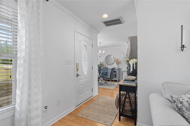 foyer entrance featuring light wood-style floors, a chandelier, crown molding, and baseboards