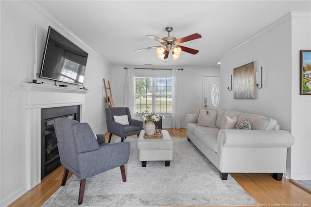 living area featuring ornamental molding, light wood-style floors, ceiling fan, a fireplace, and baseboards