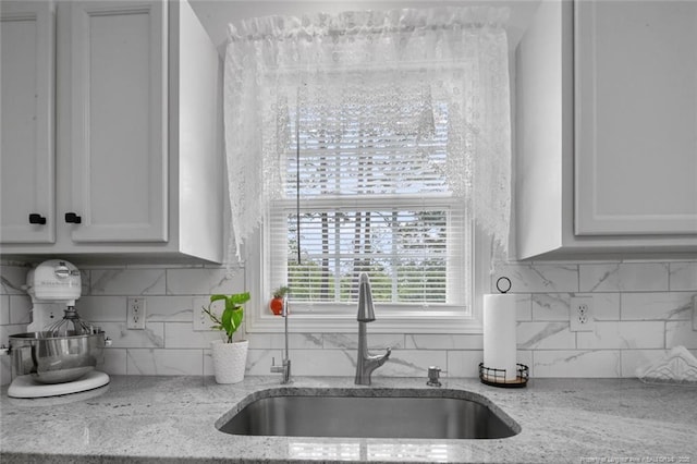 kitchen featuring a sink, light stone countertops, tasteful backsplash, and white cabinets