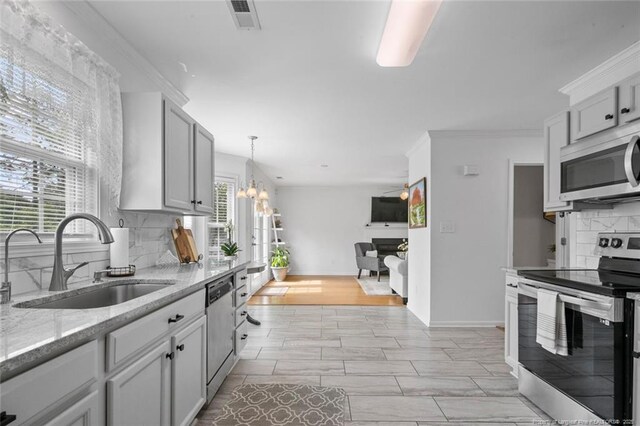 kitchen featuring appliances with stainless steel finishes, a sink, decorative backsplash, a chandelier, and light stone countertops