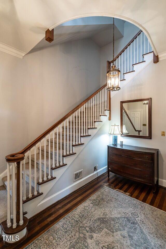 stairs with wood finished floors, baseboards, ornamental molding, and arched walkways