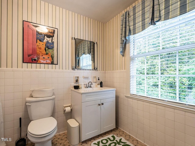 bathroom featuring tile walls, wallpapered walls, toilet, wainscoting, and vanity