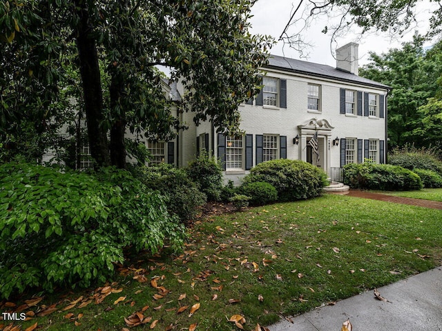 colonial-style house with a chimney, brick siding, and a front yard