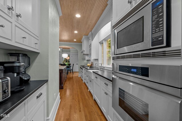 1015 Watts St, Durham, NC 27701 - kitchen featuring appliances with stainless steel finishes, arched walkways, dark countertops, light wood-style flooring, and wooden ceiling