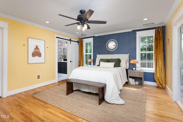 bedroom featuring crown molding, baseboards, light wood-type flooring, a barn door, and ensuite bath