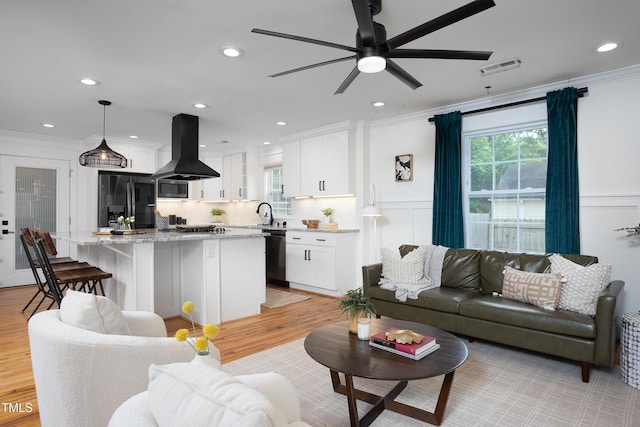 living room featuring crown molding, ceiling fan, a decorative wall, light wood-style floors, and recessed lighting