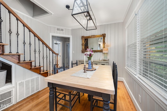 dining space featuring crown molding, light wood finished floors, and stairs