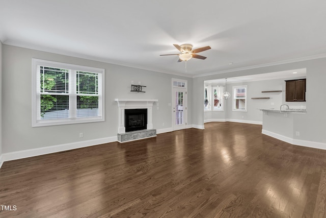 unfurnished living room featuring ceiling fan, a high end fireplace, dark wood-style floors, baseboards, and crown molding