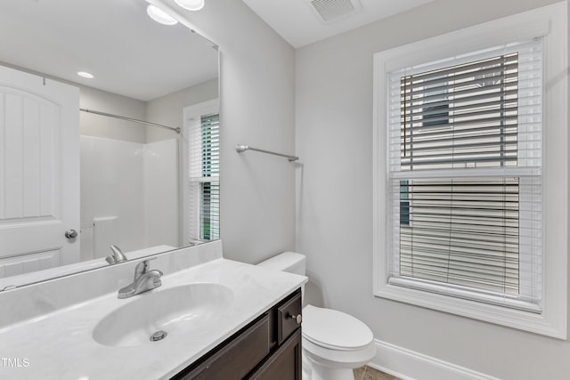bathroom featuring toilet, vanity, a shower, and baseboards