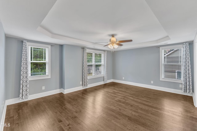 spare room with a raised ceiling, ceiling fan, baseboards, and dark wood finished floors