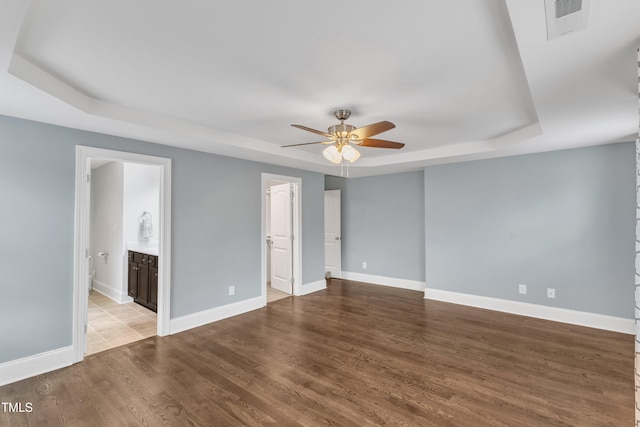 spare room featuring a raised ceiling, ceiling fan, wood finished floors, and baseboards