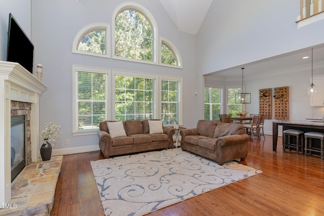 living room featuring a fireplace, wood finished floors, plenty of natural light, high vaulted ceiling, and baseboards