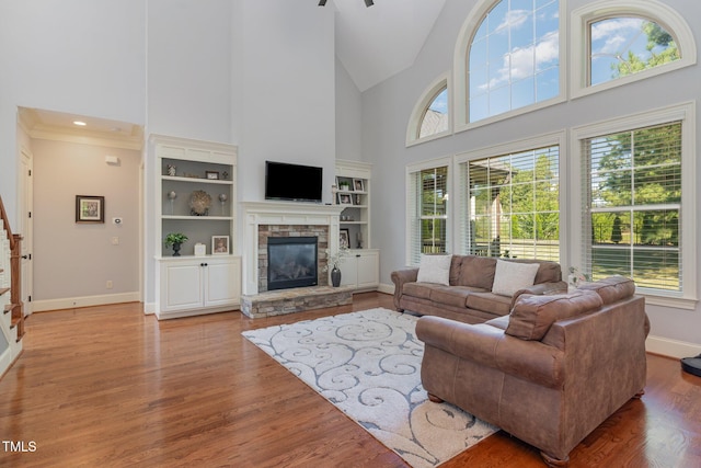 living area with high vaulted ceiling, a stone fireplace, healthy amount of natural light, baseboards, and wood finished floors