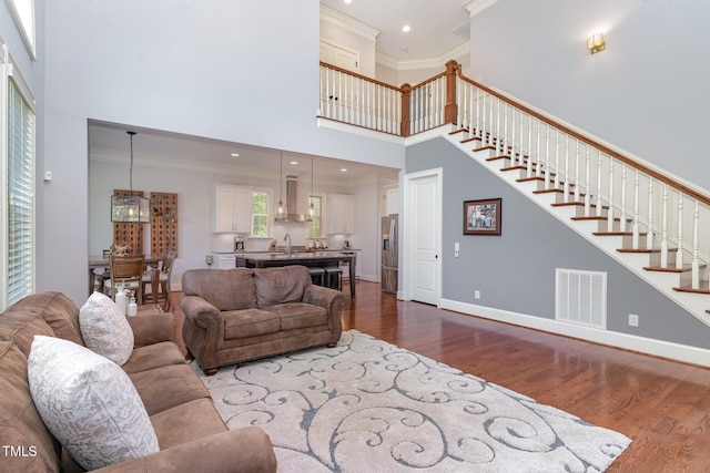 living area featuring a towering ceiling, dark wood-style floors, ornamental molding, stairs, and baseboards