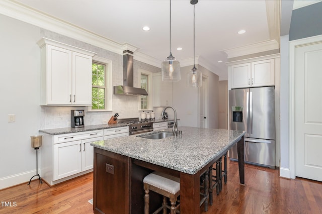 kitchen featuring appliances with stainless steel finishes, wall chimney exhaust hood, a sink, ornamental molding, and an island with sink