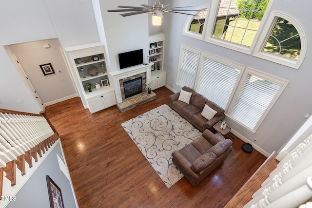 living room featuring a high ceiling, baseboards, ceiling fan, a fireplace, and wood finished floors
