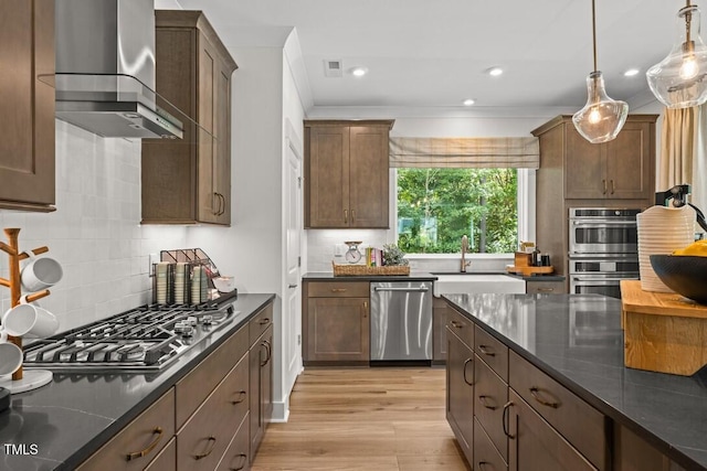 4611 Mint Leaf Ln, Raleigh, NC 27612 - kitchen with stainless steel appliances, wall chimney range hood, light wood-type flooring, tasteful backsplash, and decorative light fixtures