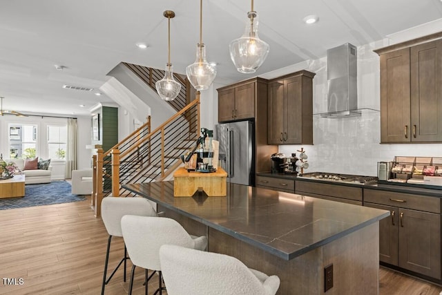 4611 Mint Leaf Ln, Raleigh, NC 27612 - kitchen featuring wall chimney exhaust hood, appliances with stainless steel finishes, wood finished floors, open floor plan, and a kitchen bar