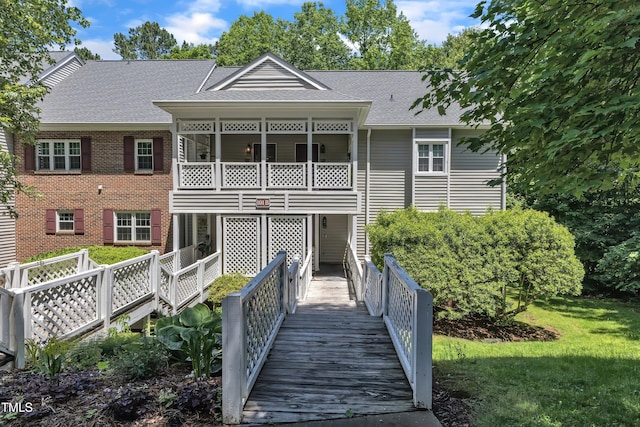 back of property featuring a shingled roof, brick siding, and a yard