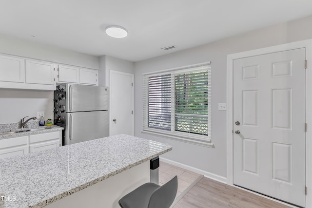 kitchen featuring freestanding refrigerator, a sink, white cabinets, light stone counters, and baseboards