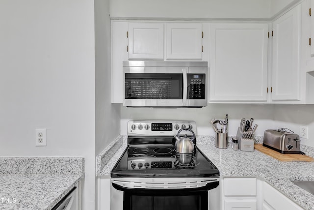 kitchen with stainless steel appliances, white cabinetry, and light stone counters
