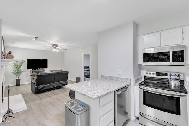 kitchen with stainless steel appliances, a peninsula, a ceiling fan, white cabinets, and light stone counters