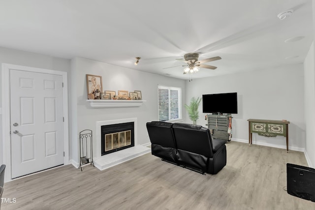 living area with light wood-style floors, a glass covered fireplace, a ceiling fan, and baseboards