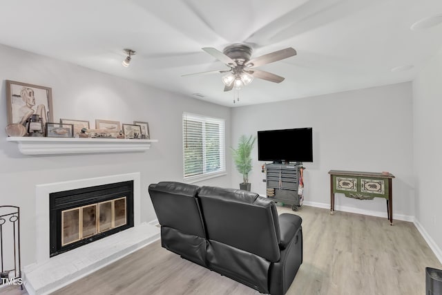 living area featuring wood finished floors, a ceiling fan, a glass covered fireplace, and baseboards