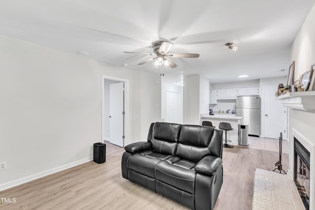 living room with ceiling fan, light wood finished floors, a fireplace with flush hearth, and baseboards