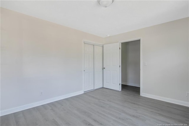unfurnished bedroom with wood finished floors, baseboards, and a closet