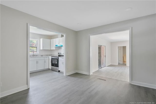 kitchen featuring stainless steel electric range oven, under cabinet range hood, a sink, white cabinets, and light wood-type flooring