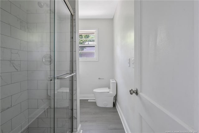 full bath featuring toilet, a stall shower, baseboards, and wood finished floors