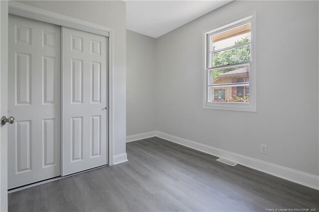 unfurnished bedroom with baseboards, dark wood-style flooring, and a closet