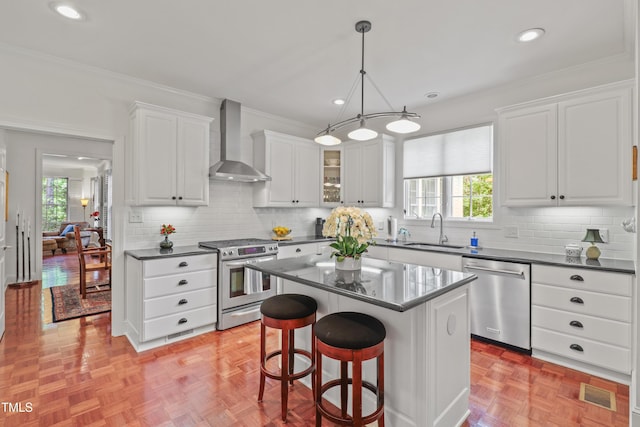 kitchen featuring appliances with stainless steel finishes, wall chimney range hood, a sink, dark countertops, and crown molding