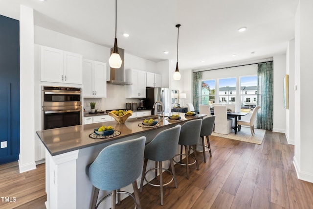 kitchen featuring stainless steel appliances, dark countertops, a kitchen island with sink, a breakfast bar, and white cabinets