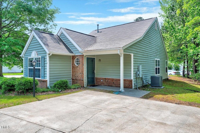 view of front of house with brick siding, cooling unit, and roof with shingles