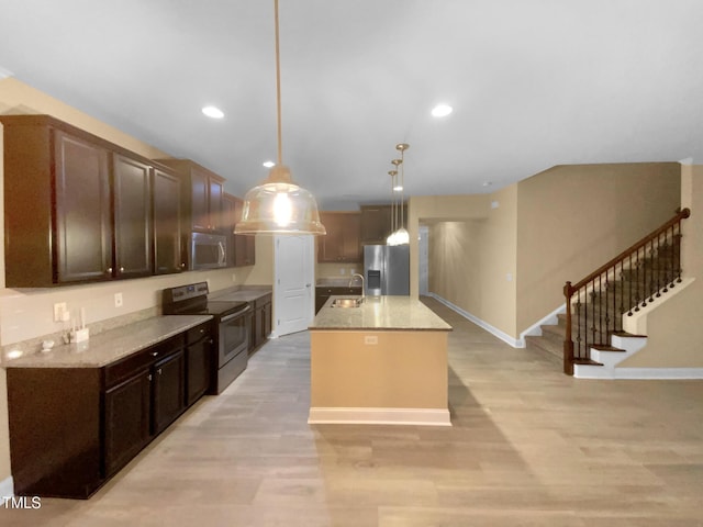 kitchen with stainless steel appliances, light wood-style flooring, pendant lighting, a kitchen island with sink, and dark brown cabinets