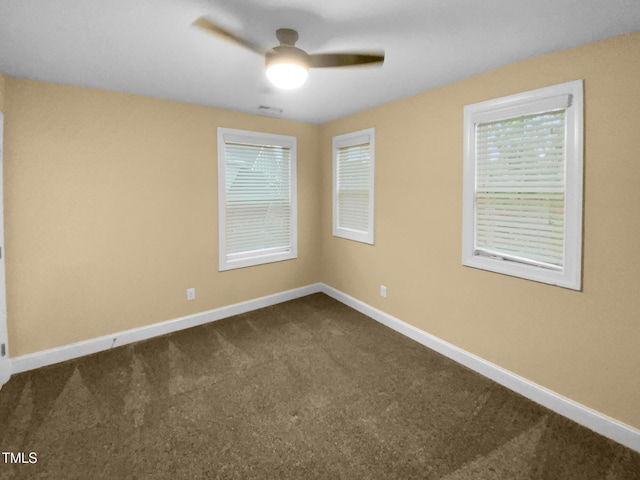 spare room featuring dark colored carpet, baseboards, ceiling fan, and plenty of natural light