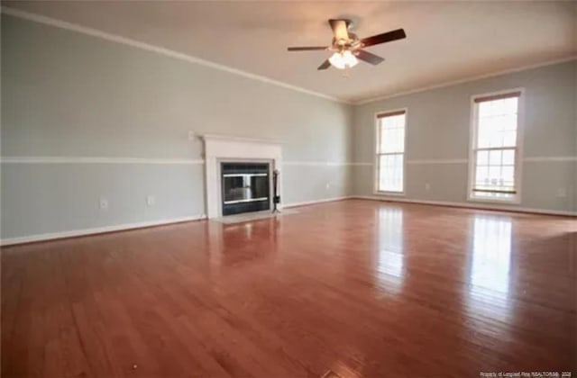 unfurnished living room featuring ornamental molding, wood finished floors, ceiling fan, a fireplace with flush hearth, and baseboards