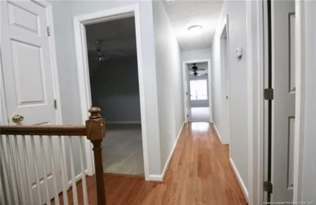 hall with light wood finished floors, baseboards, and an upstairs landing