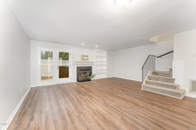 unfurnished living room featuring light wood finished floors, baseboards, stairway, and built in features