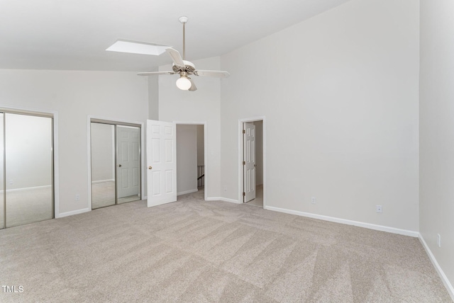 unfurnished bedroom with light carpet, multiple closets, high vaulted ceiling, baseboards, and ceiling fan