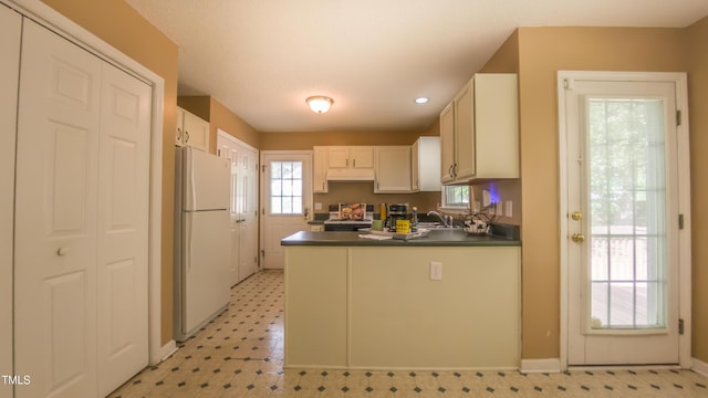 133 Parkhaven Ln, Garner, NC 27529 - kitchen featuring freestanding refrigerator, dark countertops, under cabinet range hood, light flooring, and a peninsula