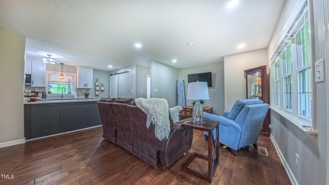 living room featuring dark wood finished floors, baseboards, recessed lighting, and a barn door