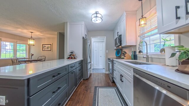 kitchen with stainless steel appliances, a sink, light countertops, a textured ceiling, and white cabinetry